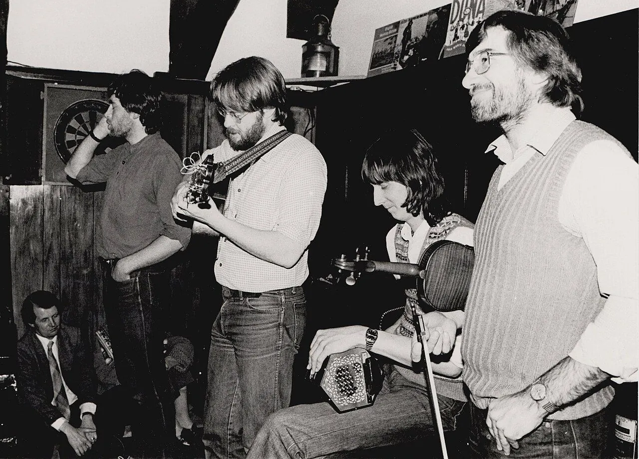 Crows (UK folk band) on stage in a London folk club in 1983 (Tony Rees photograph). L-R: Mick Ryan, vocals; James Patterson, guitar and vocals; Ralph Jordan, duet concertina; Dave Bordewey, fiddle and