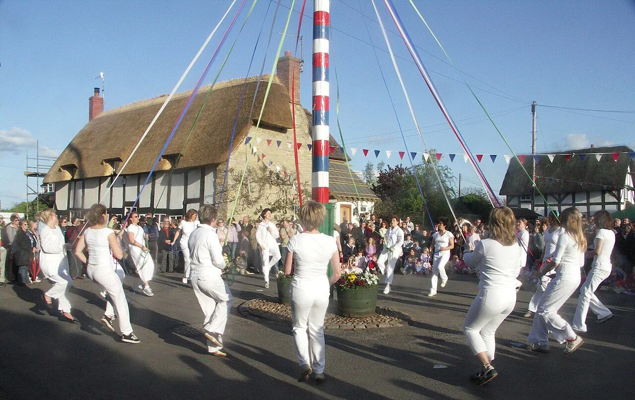 Children dancing around a ribboned maypole on a village green